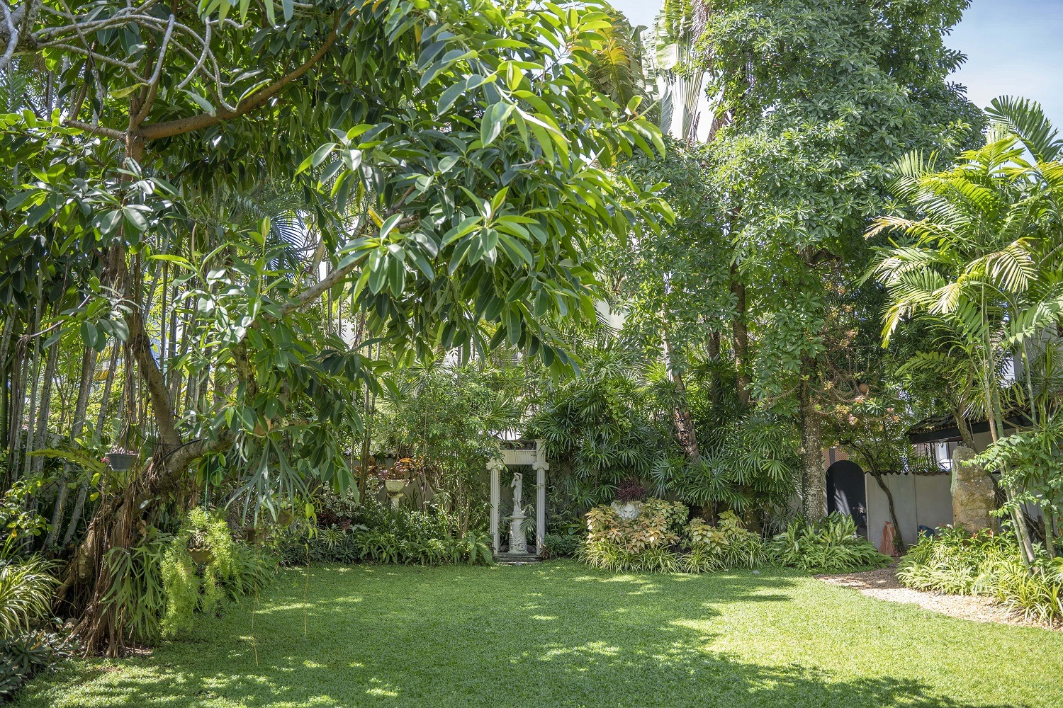 A garden view a lawn, large trees, bushes and garden sculpture