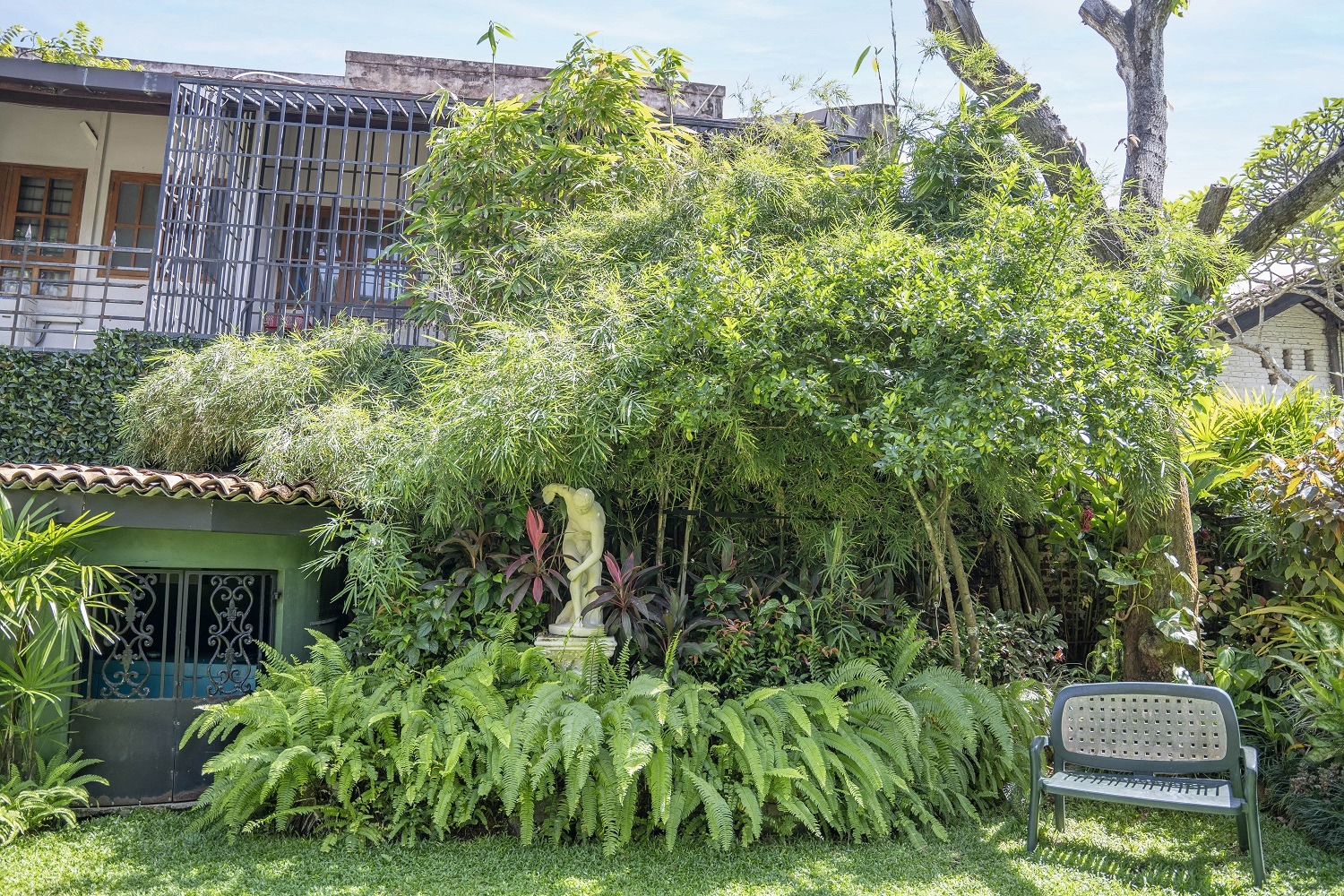 A garden with large trees, bushes and a garden sculpture