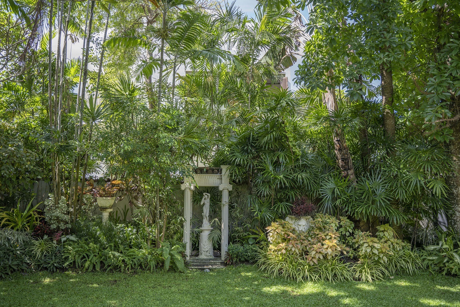 A garden with large trees, bushes and a garden sculpture